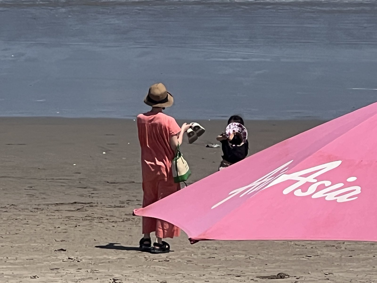 ピンクの傘が並ぶビーチを歩く親子
