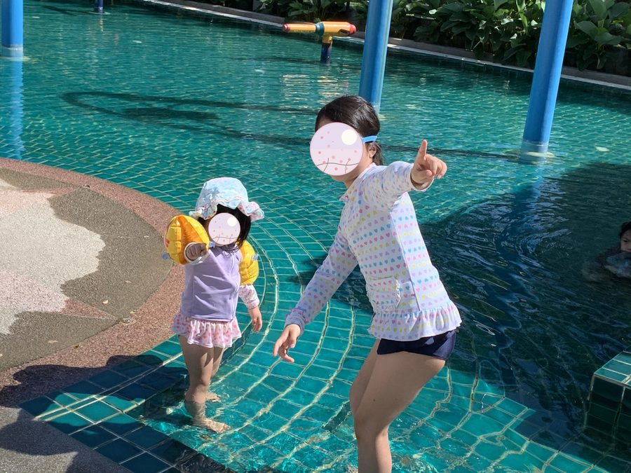 水遊び場で元気にポーズ。奥では妹も浮き輪をつけて水に入っています